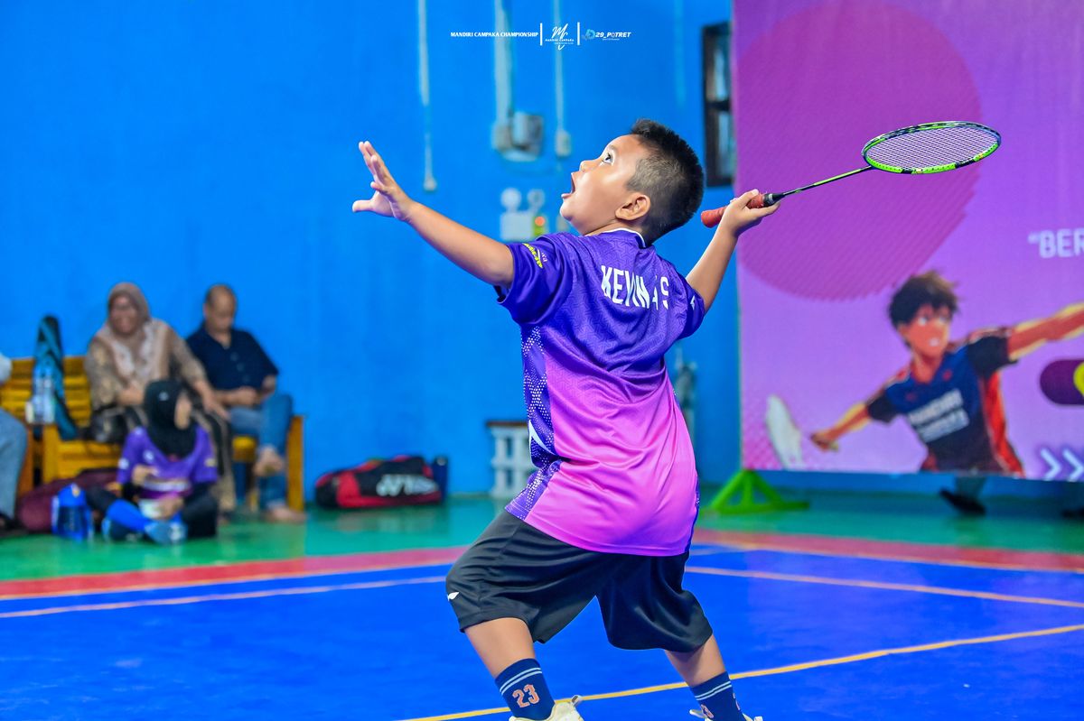 Atlet mengangkat raket bersiap memukul kok tinggi